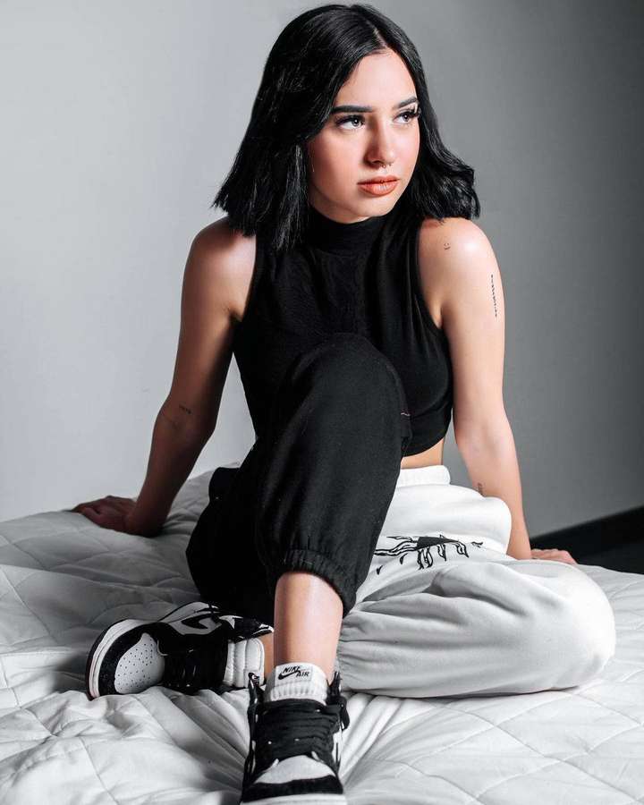 Giovane donna in abito nero seduta su letto bianco con scarpe da ginnastica — Domelipa Sfondi