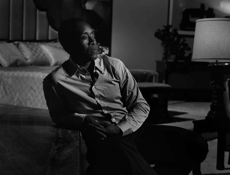 Mies istuu yksin pimeässä makuuhuoneessa, näyttäen mietteliäältä lampun valossa. — Don Cheadle Taustakuvat