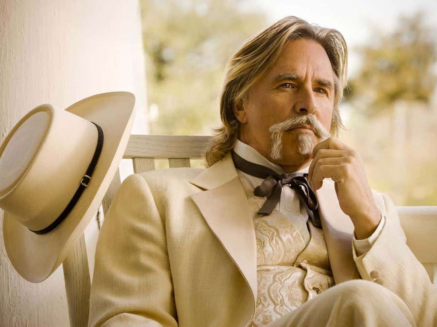 A man with a mustache sits on a bench wearing a cream suit and hat. — Don Johnson Wallpaper