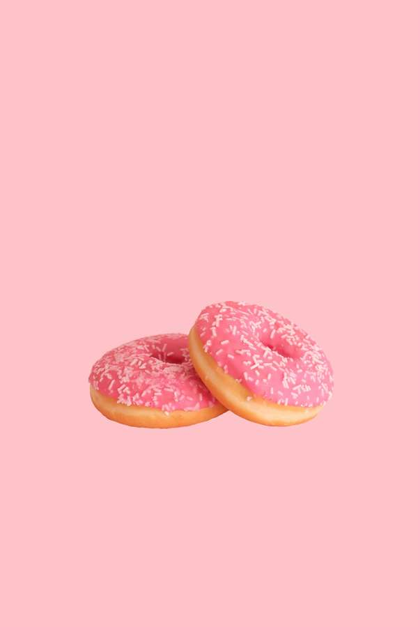 Dos donuts glaseados rosas con chispas blancas sobre un fondo rosa pastel. — Donas Fondos de pantalla