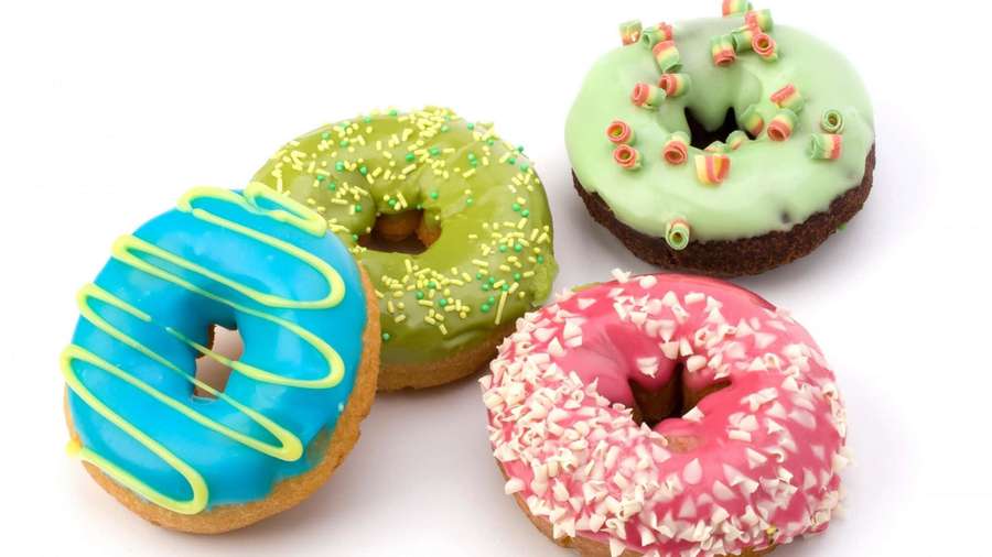 Four colorful glazed donuts with sprinkles on a white background. — Donuts Background