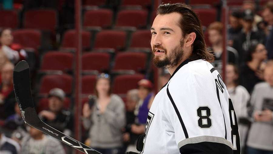 Hockey player in white jersey number 8 smiling with stick on ice rink. — Drew Doughty Wallpaper