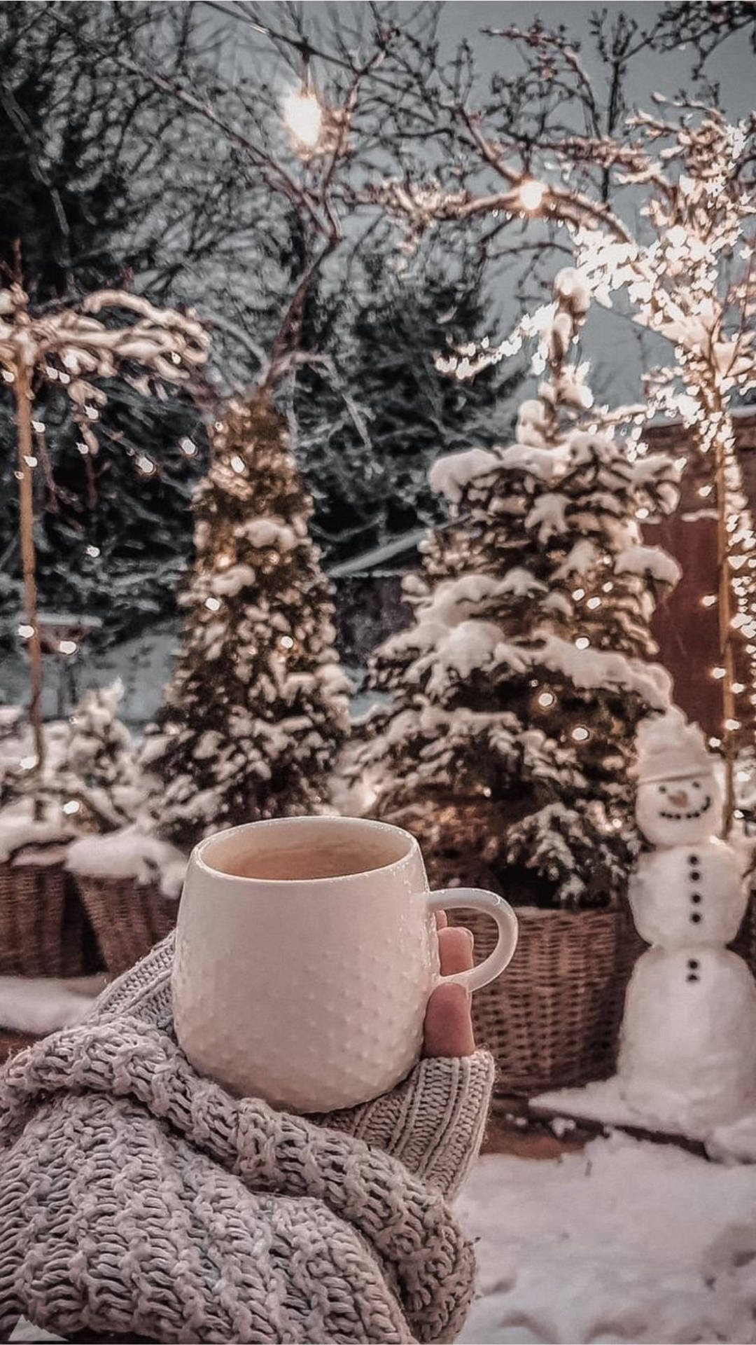 Hand som håller en mugg insvept i en stickad tröja i en snöig trädgård med snögubbar och ljus. — Dricka Bakgrundsbilder
