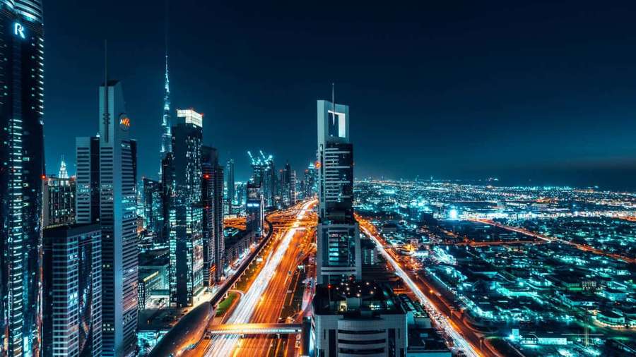 Futuristic city skyline at night with glowing towers and light trails from moving vehicles. — Dubai Background