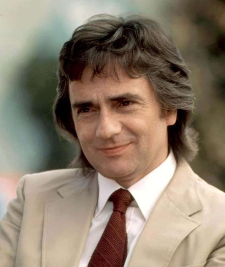 Man in beige suit and red tie smiling outdoors — Dudley Moore Picture