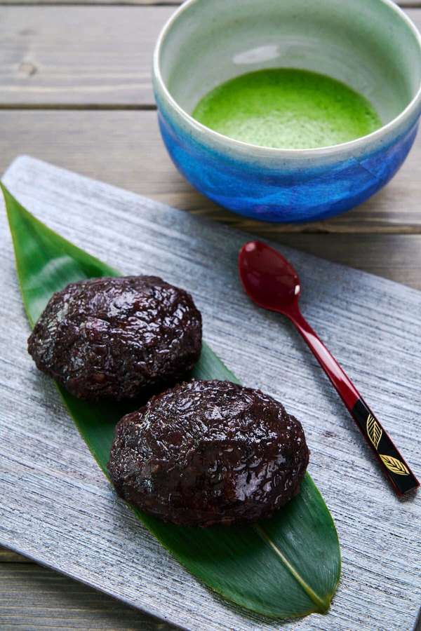 Dos mochi oscuros sobre hoja de bambú con té matcha y cuchara roja sobre madera — Dulces japoneses Fondos de pantalla