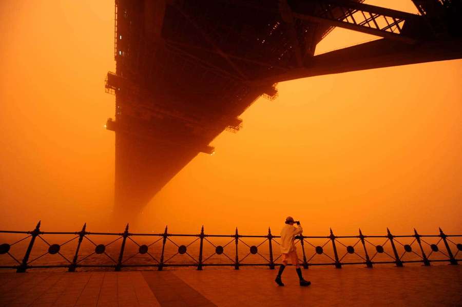 Person walking under a bridge in orange haze at dusk. — Dust Storm Wallpaper