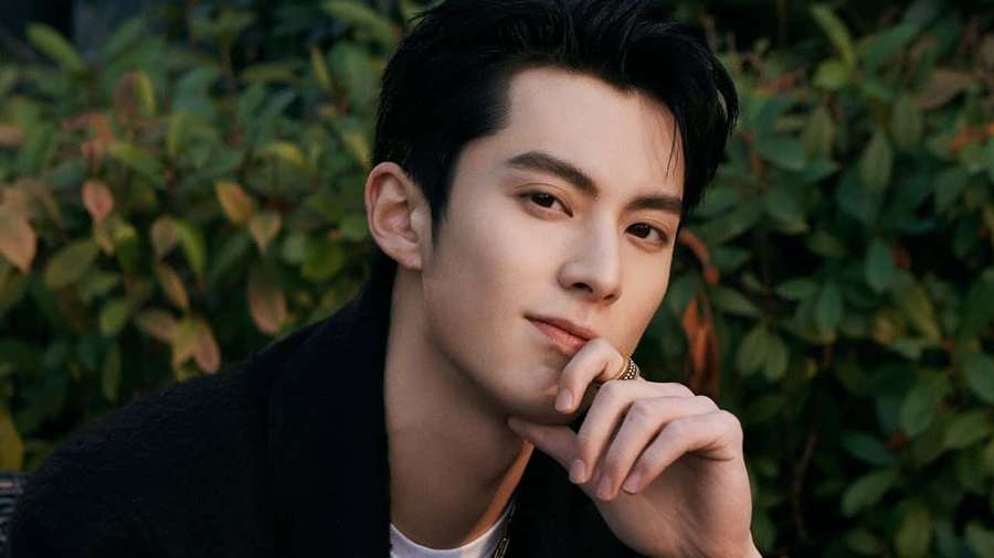 Junger Mann in schwarzer Jacke posiert nachdenklich im Freien mit grünem Laub im Hintergrund. — Dylan Wang Wallpaper
