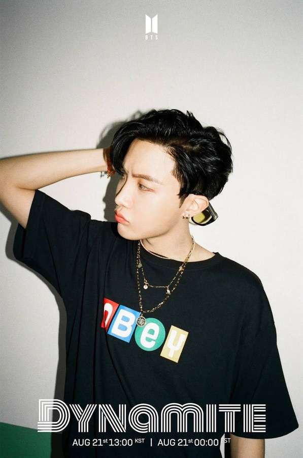 Junger K-Pop-Künstler in schwarzem T-Shirt mit bunten Buchstaben und mehrlagigem Schmuck, der im Studio posiert. — Dynamit Wallpaper