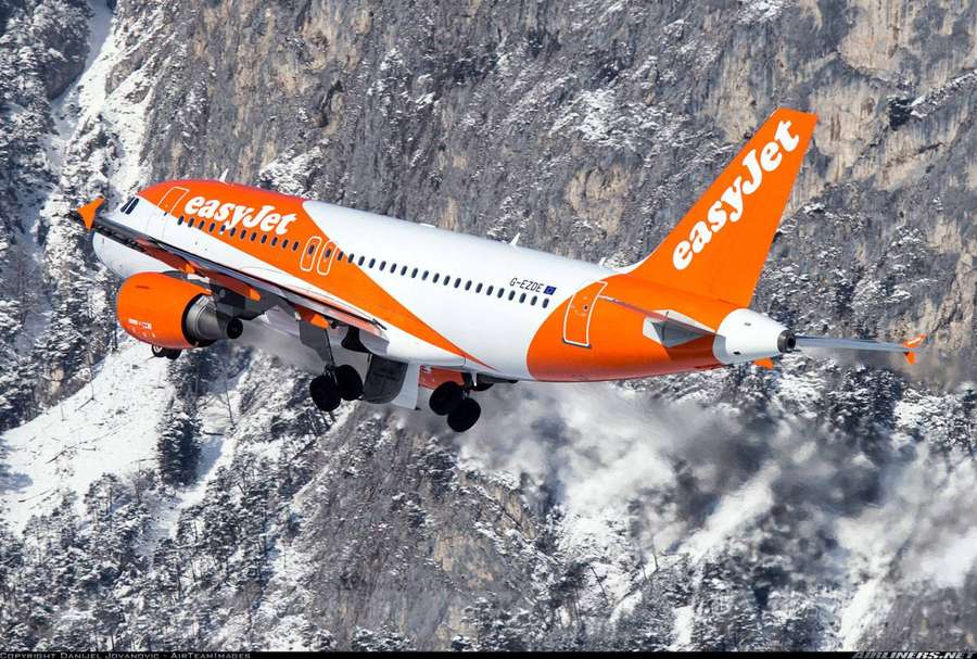 Orange-weißes easyJet-Flugzeug fliegt tief über schneebedeckte Berge. — Easyjet Bilder