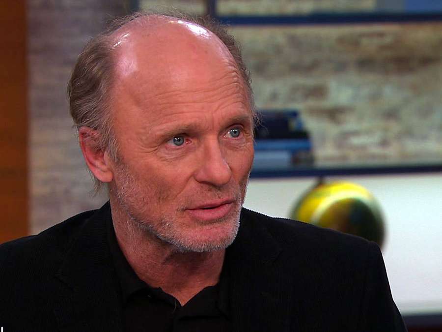 Ein kahl werdender Mann mit grauem Bart und blauen Augen in einer schwarzen Anzugjacke während eines Interviews. — Ed Harris Bilder