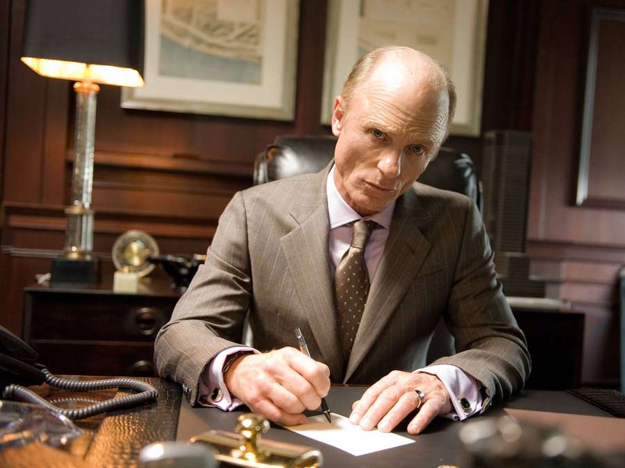 A man in a suit signs a document at a wooden desk in an office. — Ed Harris Wallpaper