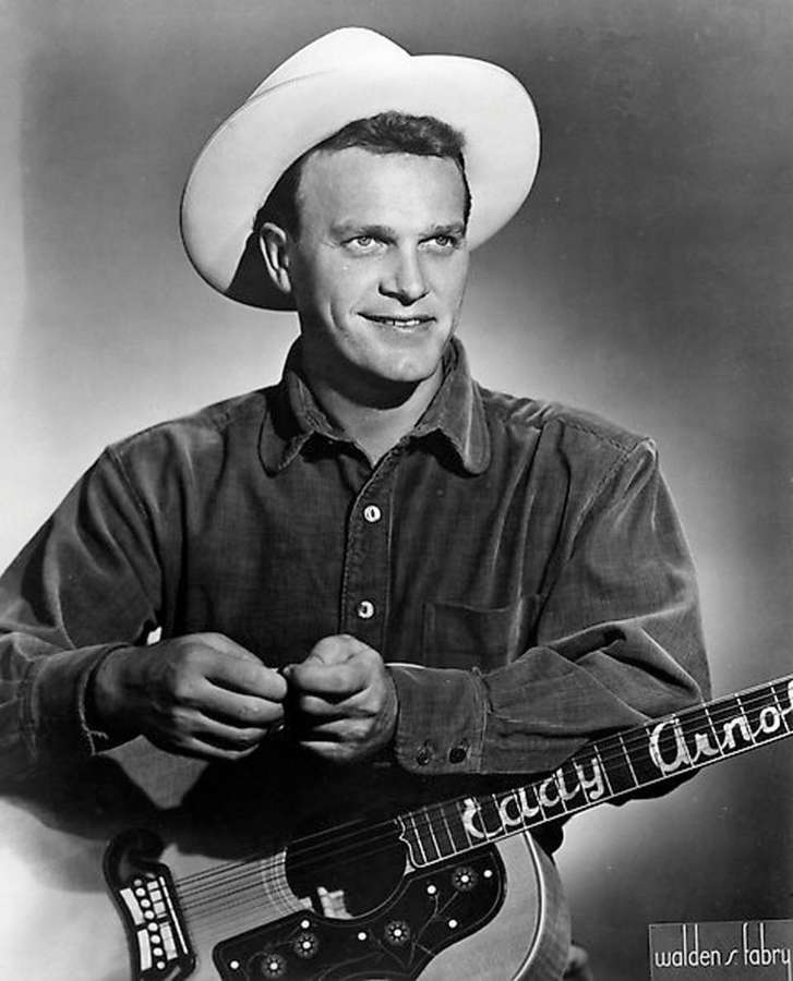 A smiling cowboy musician holding a guitar in a studio portrait. — Eddy Arnold Wallpaper