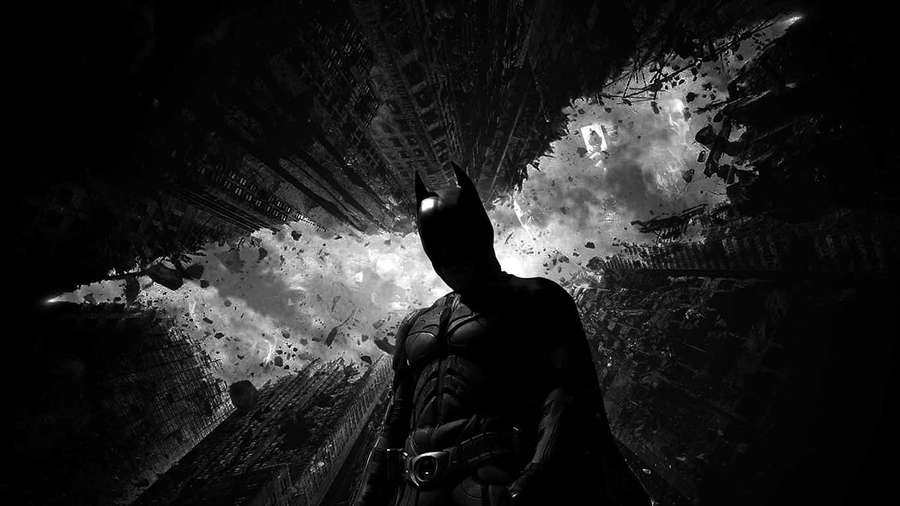 Batman em um ambiente urbano escuro com destroços explodindo ao seu redor. — Edifícios Papéis de Parede