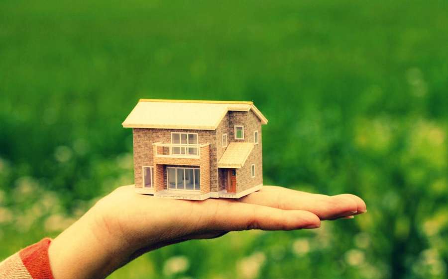 Mano sosteniendo una pequeña casa modelo en un campo de hierba. — Eficiente Fondos de pantalla