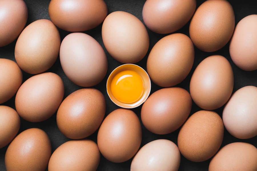 A cracked egg yolk surrounded by whole brown eggs on a dark surface. — Egg Background