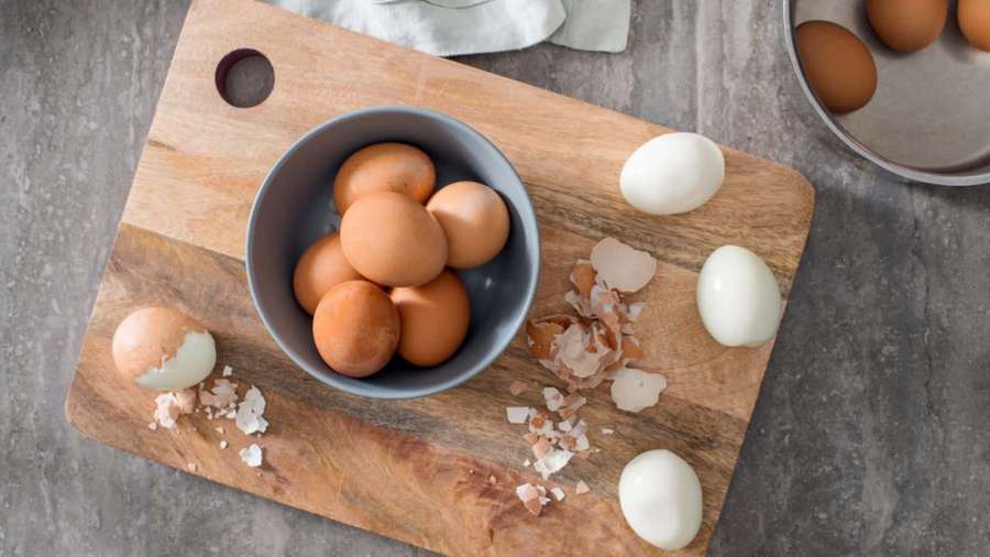 Brown and peeled white eggs on a wooden cutting board with shells scattered around. — Egg Picture
