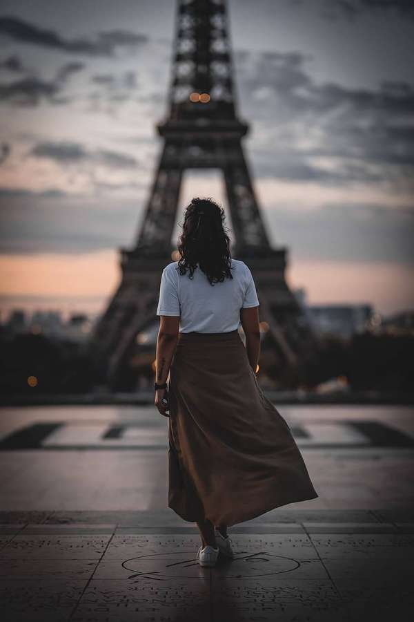 Eine Frau geht bei Sonnenuntergang in Paris auf den Eiffelturm zu. — Eiffel Hintergrundbild