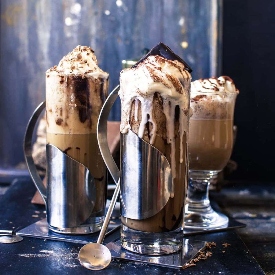 Drei Schokoladen-Milchshakes mit Schlagsahne und Schokoladenraspeln in metallischen Gläsern. — Eiskaffee Bilder