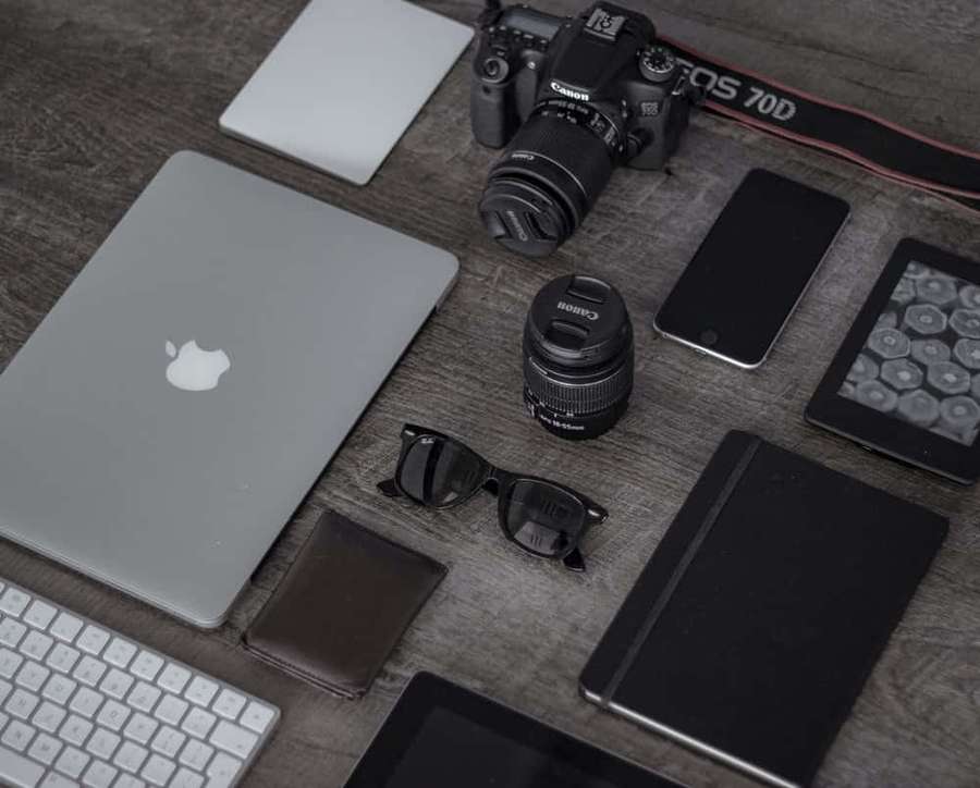 Modern tech gadgets on a wooden desk including laptop camera phone and sunglasses. — Electronics Background