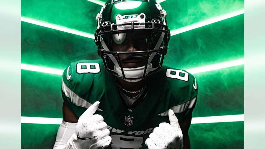 Football player in green uniform giving two thumbs up against neon green background. — Elijah Moore Wallpaper