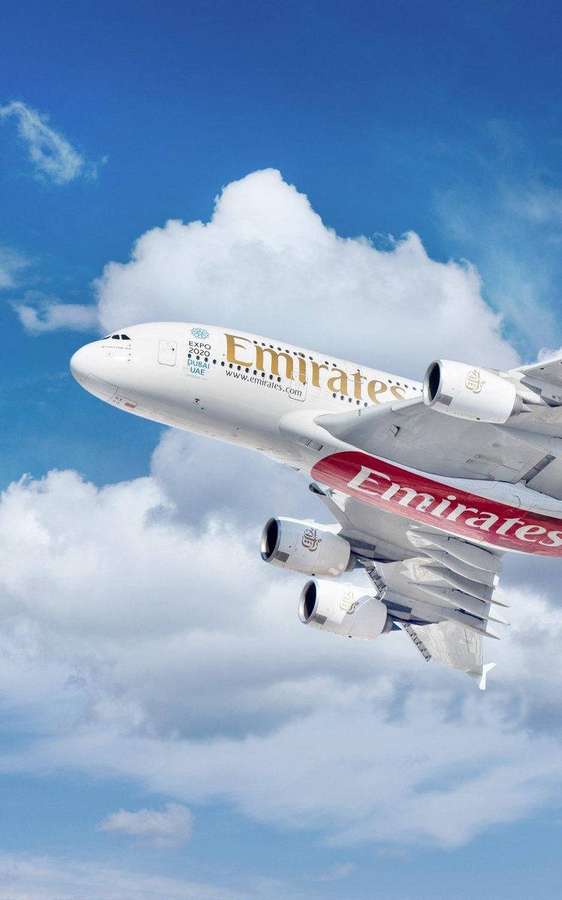 Emirates Airbus A380 lentää korkealla pörröisten valkoisten pilvien yläpuolella kirkkaansinisellä taivaalla. — Emiraatit Taustakuvat