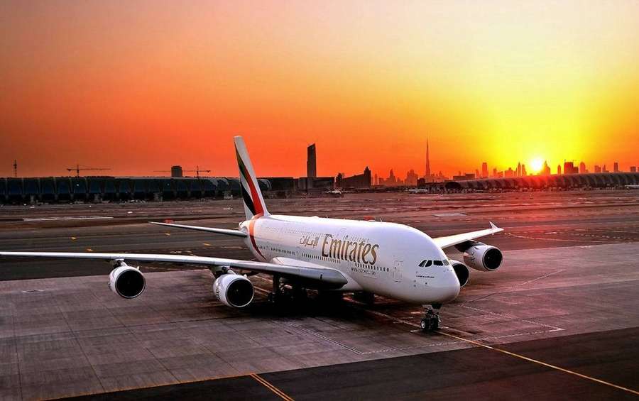 Emirates A380 airplane on tarmac at sunset with city skyline in background — Emirates Wallpaper