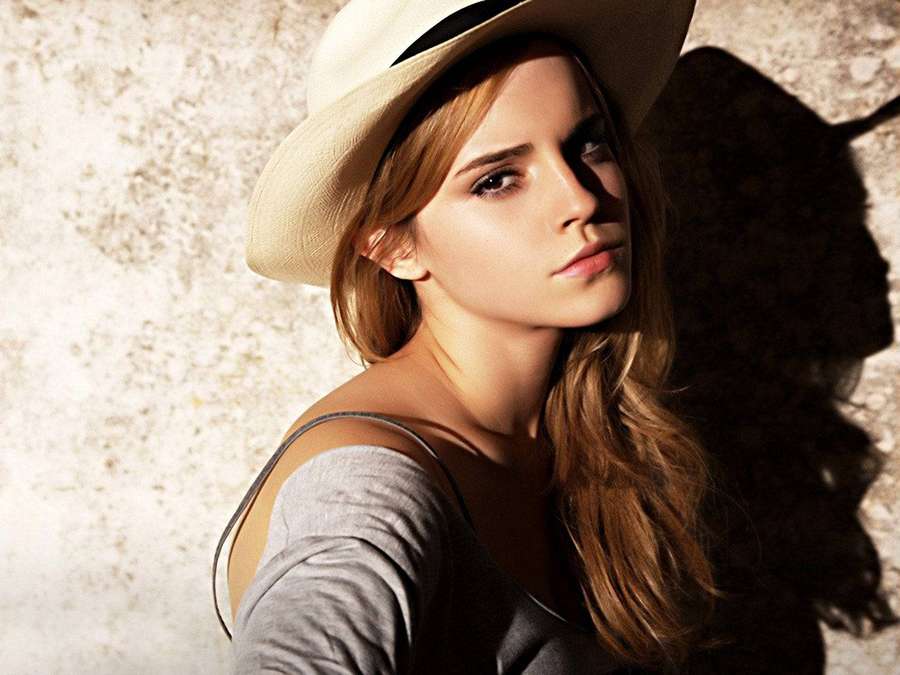 Woman in beige hat and gray top standing against textured wall with strong shadow. — Emma Watson Wallpaper