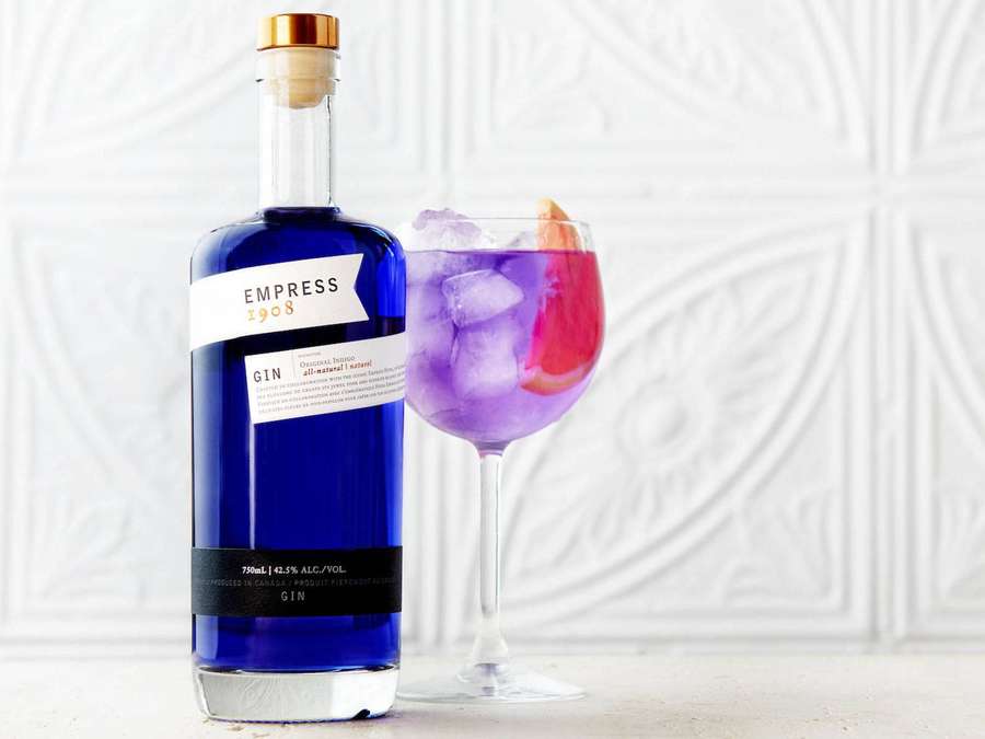 Blue gin bottle and purple cocktail with ice and citrus garnish on a white surface. — Empress Wallpaper