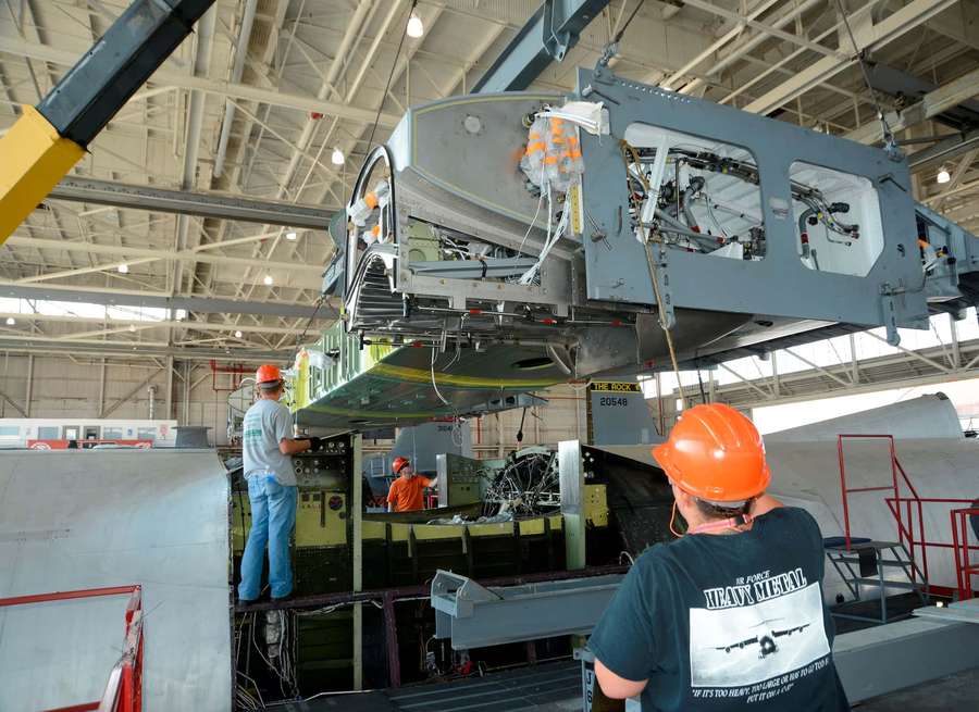 Technicians assemble a military aircraft inside a large industrial hangar. — Engineer Background