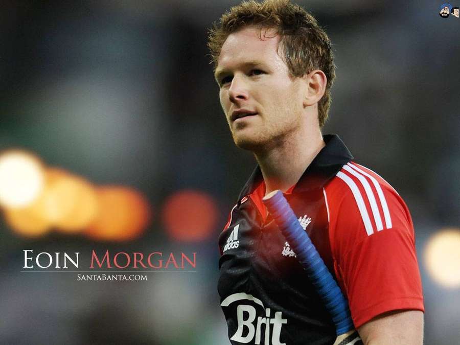 Cricketspieler Eoin Morgan in rot-schwarzer Uniform hält Schläger bei Nachtspiel. — Eoin Morgan Wallpaper