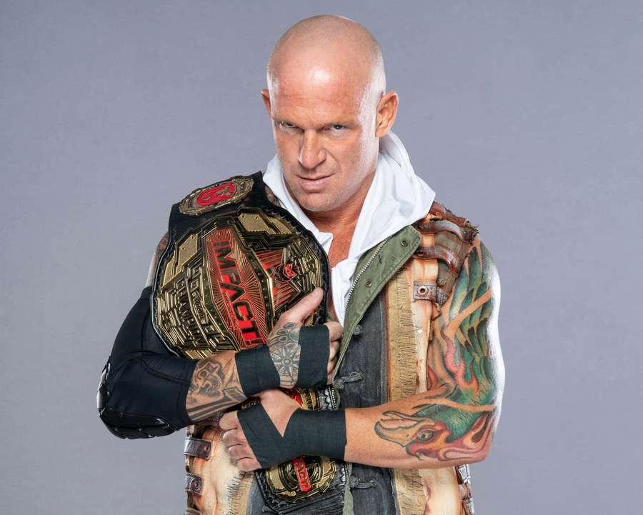 A bald tattooed wrestler holding an Impact championship belt with a serious expression. — Eric Young Wallpaper