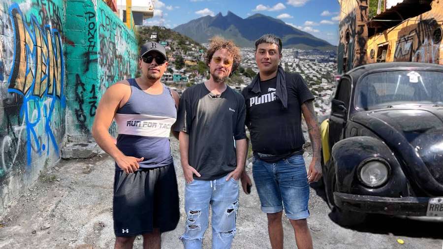 Tres hombres posando junto a un clásico VW Beetle negro en una calle cubierta de graffiti con montañas al fondo. — Escarabajo Fondos de pantalla