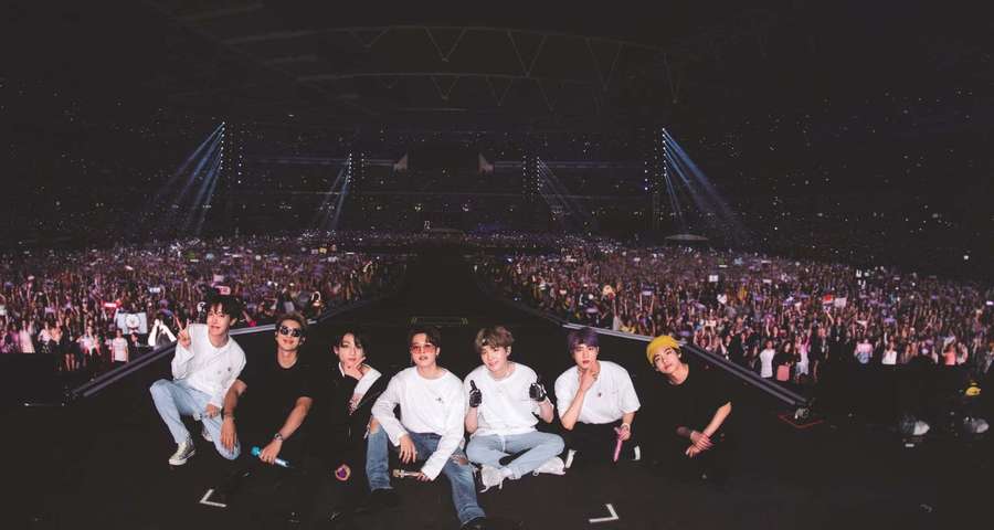 Siete artistas posan en un escenario de concierto frente a una gran multitud que vitorea por la noche. — Escenario de Bts Fondos de pantalla