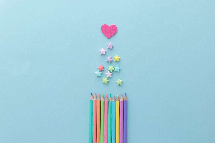 Lápices de colores con caramelos estrella cayendo hacia un corazón rosa sobre fondo azul. — Escritorio Pastel Fondos de pantalla