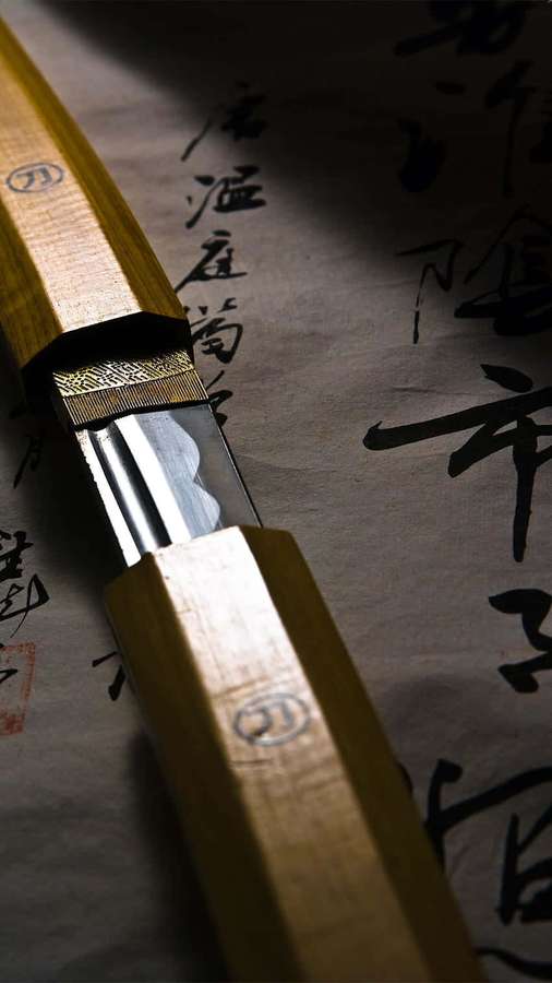 Primer plano de un cuchillo japonés sobre papel de caligrafía con mango de madera y hoja de metal. — Espada Samurai Fondos de pantalla