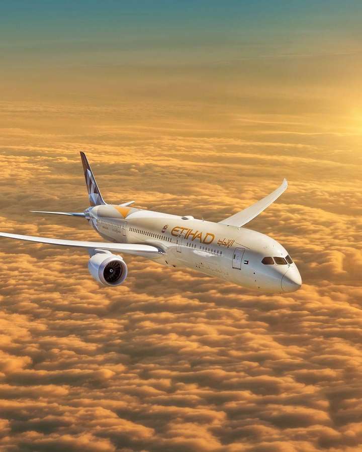 Etihad Airways plane flying above golden clouds at sunset. — Etihad Wallpaper