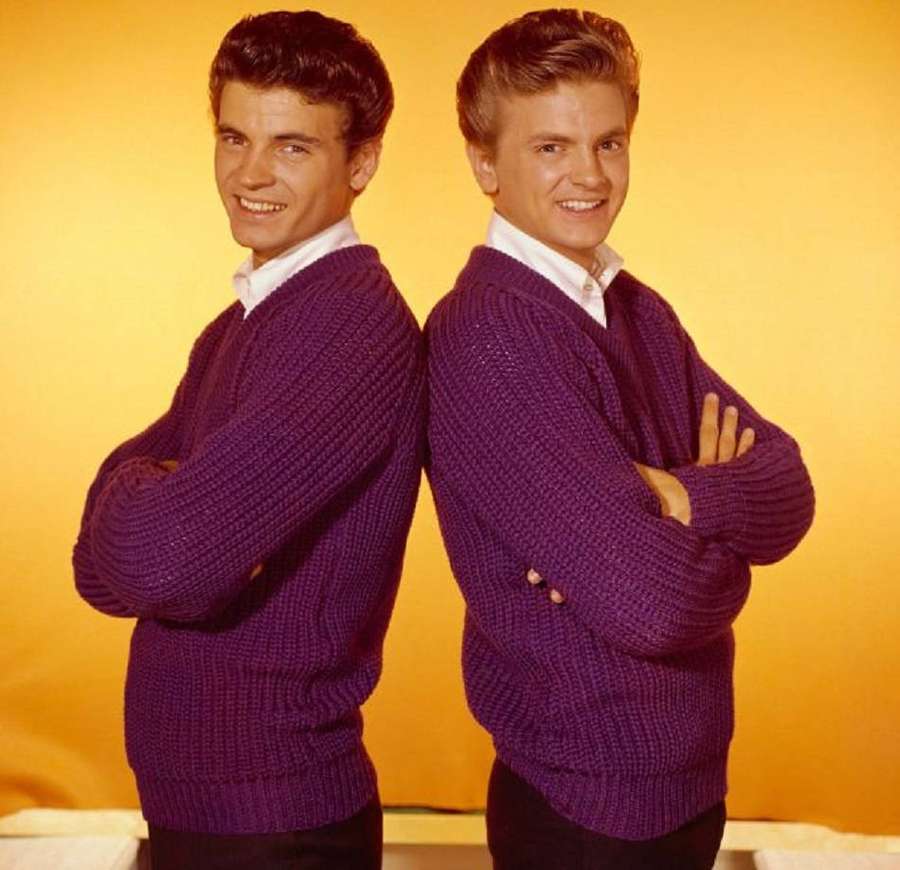 Two men in purple sweaters smiling while standing back to back. — Everly Brothers Wallpaper