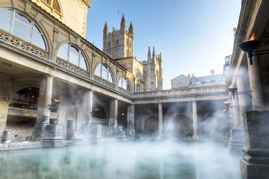 Ancient Roman bath with steam rising under Gothic architecture on a sunny day. — Exeter Wallpaper