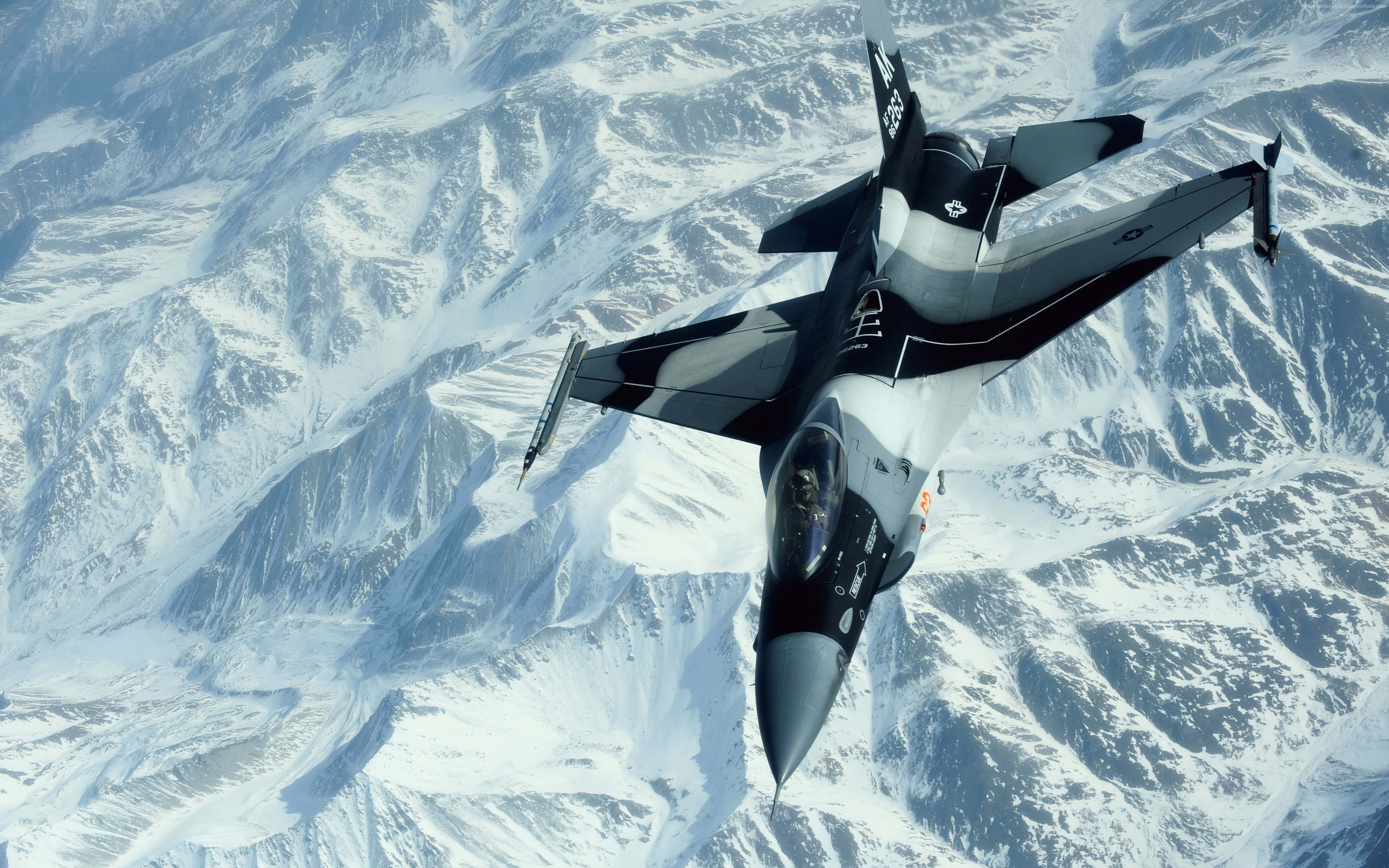 Fighter jet flying over snowy mountain range — F-16 Wallpaper