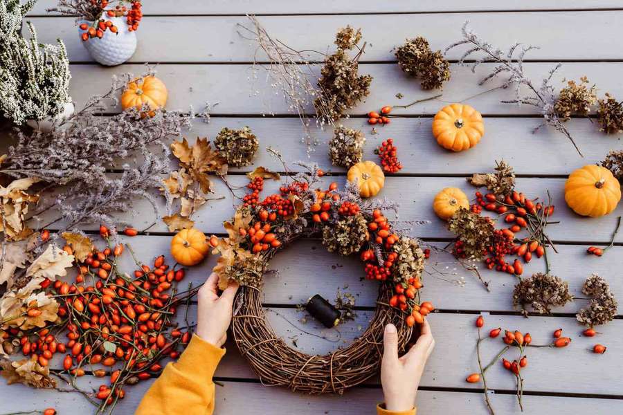 Person assembling a fall wreath with pumpkins and berries on a wooden surface. — Fall Wreath Wallpaper