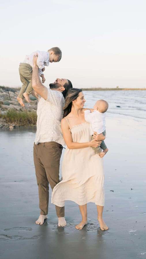 A smiling family of four enjoying a beach sunset together barefoot in shallow water. — Family Beach Wallpaper