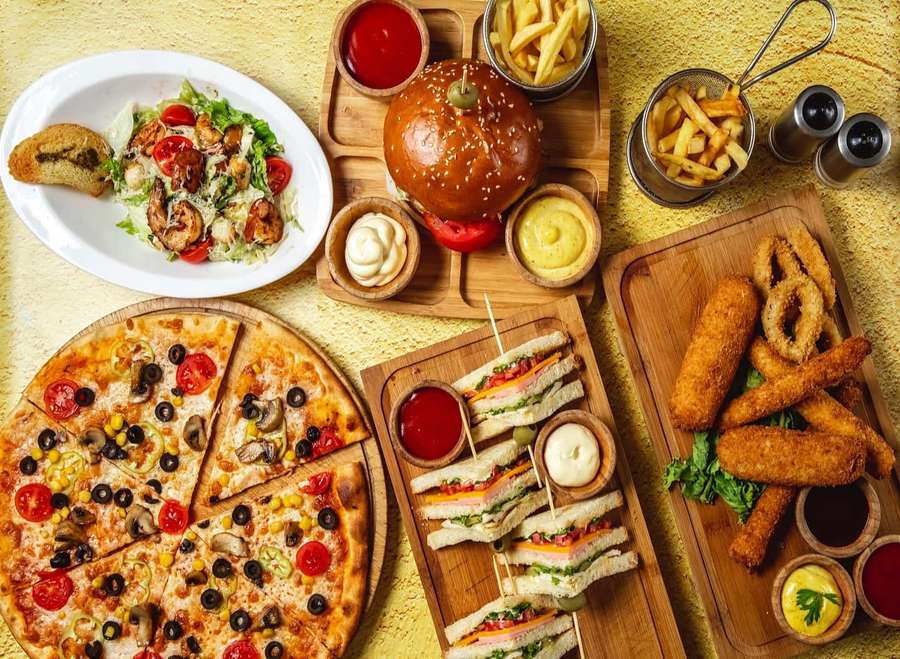 A colorful spread of pizza burger sandwiches and fries with dipping sauces on wooden boards. — Fast food Picture