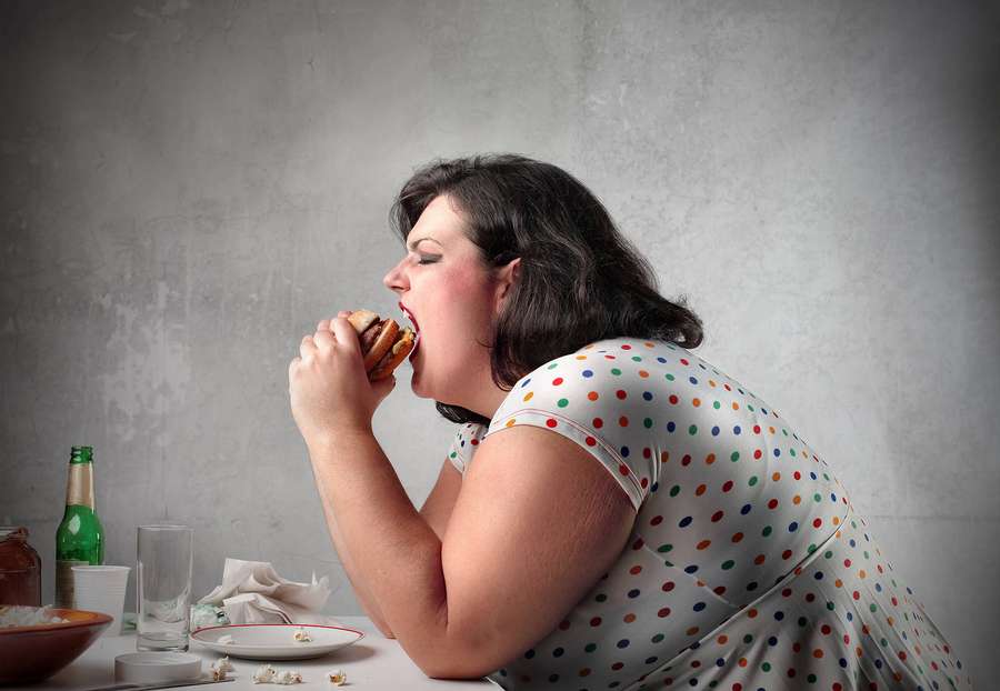 Woman in polka dot dress eating large burger at messy table with beer bottle. — Fat Girl Background