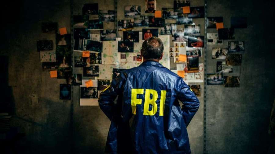 Agente FBI in giacca blu di fronte a parete ricoperta di foto e appunti — Fbi Sfondi