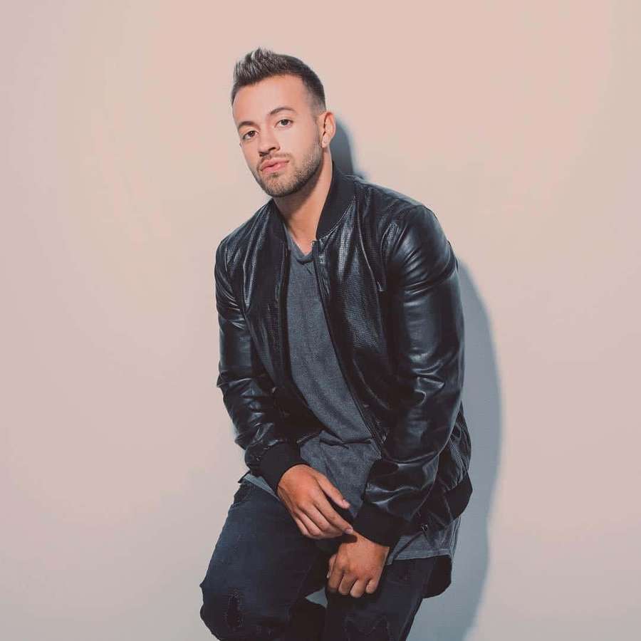 A man in a black leather jacket posing against a pink studio wall. — Feid Wallpaper