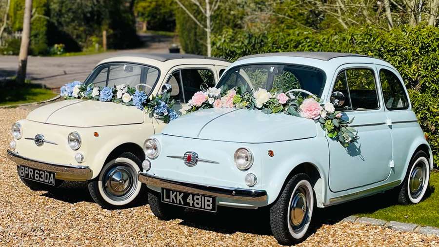 Zwei vintage Fiat 500 Autos, dekoriert mit Blumen, auf Kies in der Nähe von grünen Hecken geparkt. — Fiat Bilder