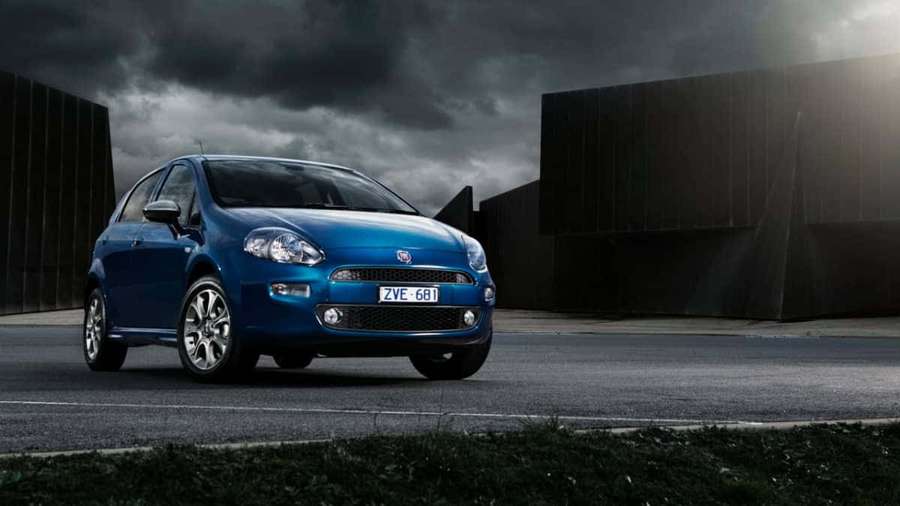 Fiat Punto azul estacionado sobre asfalto bajo cielo tormentoso cerca de edificios industriales. — Fiat Punto Fondos de pantalla