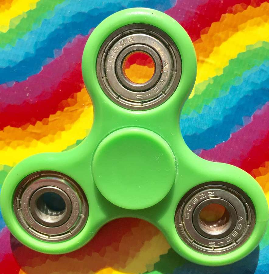 Ein grüner Fidget Spinner mit ABEC-5-Lagern auf einem Regenbogen-gemusterten Hintergrund. — Fidget Bilder
