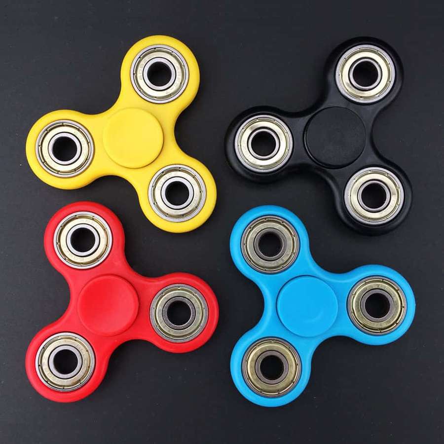 Four fidget spinners in red yellow blue and black on a dark background. — Fidget Toys Background